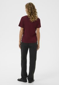 Burgundy t-shirt with short sleeves, relaxed fit. Paired with black straight-leg jeans, textured fabric, and black shoes. Simple design.