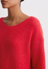 Red knit sweater with a loose fit, wide neckline, and textured pattern. Fabric appears soft and warm, showcasing ribbed detailing on sleeves.