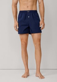Pantaloni da bagno blu navy con vita elastica, dettaglio a bottone e vestibilità ampia. Realizzati in materiale leggero e ad asciugatura rapida.
