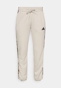 Lys beige joggebukser laget av myk stoff, med snor i midjen og svarte sidelabber med leopardmønster.