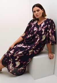 Robe maxi fluide en violet foncé avec des motifs abstraits roses et crème. Dotée d'un décolleté en V et de larges manches pour un ajustement décontracté. Tissu léger.