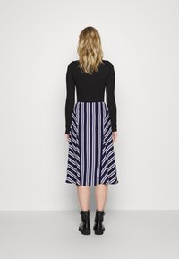 Černý dlouhý rukáv top spárovaný s sukní ke kolenům v námořnické modři, která má bílé vertikální pruhy. Model nosí černé kotníkové boty.