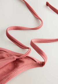Roze beha van soepel materiaal, met dunne bandjes en decorative stiksels langs de randen. De bandjes liggen plat tegen een witte achtergrond.