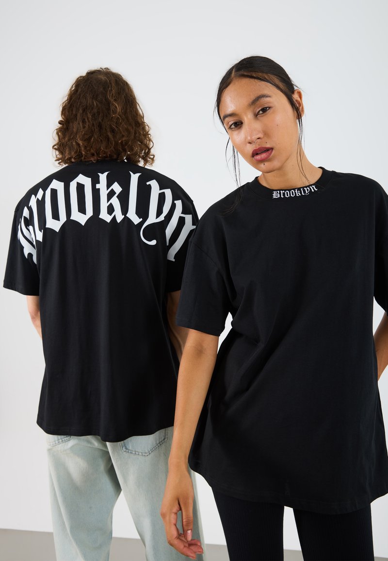 Svart oversized t-shirt med "Brooklyn" i fet vit gotisk stil på baksidan och en mindre version på framsidan vid kragen. Tillverkad av bomullsmaterial.