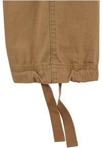 Khaki kangast käeosa elastse kogumisega, koos kahe seotud nööriga, mis võimaldab reguleerida sobivust. Sile tekstuur ja korralik õmbluse detail nähtav.