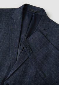 Giacca di abito in blu navy con texture, caratterizzata da un sottile motivo a scacchi, rever a rotondo e dettagli con quattro bottoni sui polsini. Interno foderato in tessuto scuro.