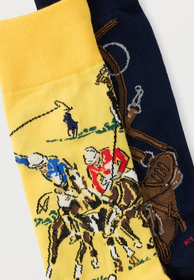 Δύο διπλωμένες κάλτσες, η μία κίτρινη με σκηνή αγώνα πόλο και η άλλη ναυτικό μπλε με σχέδιο καφέ ρόπαλου πόλο.
