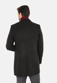 Cappotto in lana nera con una vestibilità su misura, rever a lappetto e accentuazione del colletto in bordeaux. Texture liscia con cuciture dettagliate lungo le cuciture.