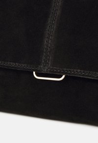 Clutch in suede nera con un accento in metallo dorato. Presenta linee pulite, una superficie liscia e cuciture dettagliate lungo i bordi.
