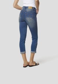 Denim-Capri-Jeans mit ausgewaschenem Blauton, umgeschlagenem Saum und besticktem Detail am linken Bein. Verfügt über normale Gesäßtaschen und ein Lederpatch.