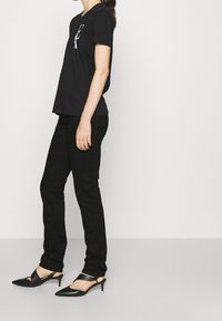 Svart bomullströja med korta ärmar och tryckt logotyp, i kombination med svarta slim-fit jeans och svarta spetsiga slingback-skor.