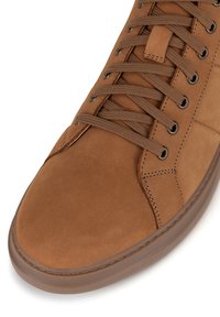 Hnědé semišové tenisky s odpovídajícími hnědými tkaničkami a kovovými očky, podrobným prošíváním a silnou gumovou podrážkou.