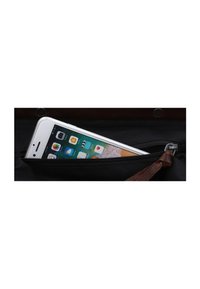 Pochette zippée noire avec un accent en cuir marron, partiellement ouverte pour révéler un smartphone argenté affichant une interface d'application à l'intérieur.