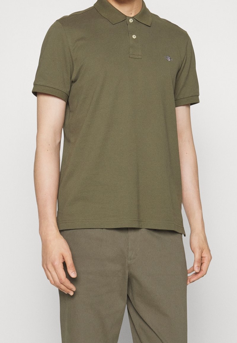 Polo shirt vert olive en coton, avec un col classique, des manches courtes et un petit logo brodé sur la poitrine.