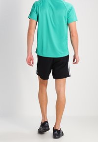Men's athletic outfit featuring a teal short-sleeve moisture-wicking shirt and black shorts with white side stripes, paired with black running shoes.