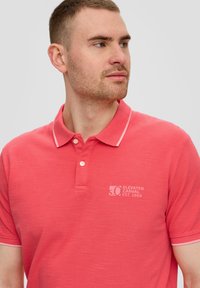 Pe coralist polo särk, mis on valmistatud pehmest puuvillast, kahe nööbiga kraega, kontrastsete valgete ääristega ja rinnal toon-toonis logoga.
