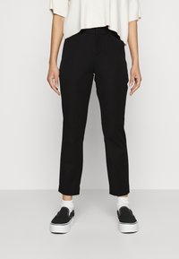 Pantalones negros ajustados con un corte slim, con una textura suave y una cintura de altura media, acompañados de zapatos negros tipo slip-on y calcetines blancos.