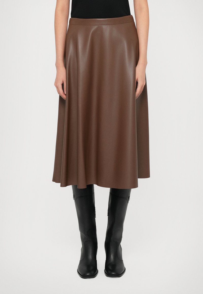 Brown faux leather midi skirt with a flared design; smooth texture and wide waistband; paired with knee-high black boots.