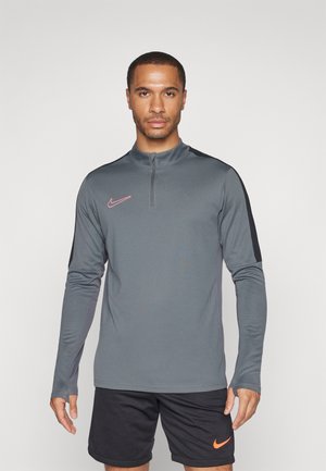 Graues langärmliges Sportoberteil mit Viertelreißverschluss, das schwarze Akzente an den Schultern und ein pinkes Nike-Logo auf der linken Brust hat.