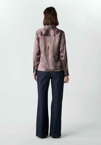 Kurzärmliges braunes Satinhemd mit langen Ärmeln und Knopfmanschetten, kombiniert mit einer hoch taillierten dunkelblauen Bootcut-Jeans. Sauberes, minimalistisches Design.