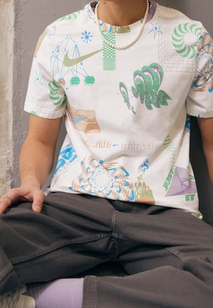 T-shirt blanc à manches courtes avec des motifs graphiques colorés en vert, bleu et marron, un col rond et une coupe décontractée.