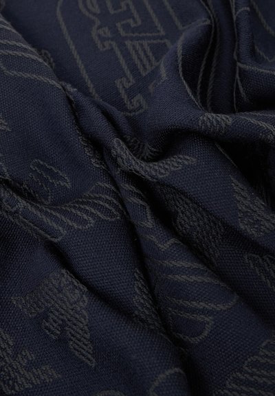 Tissu bleu foncé avec des motifs texturés tissés et des lettres, montré en gros plan avec des plis et des froissements visibles.