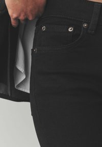 Los jeans de mezclilla negra presentan un diseño ajustado con una textura suave, costuras visibles y detalles de metal.