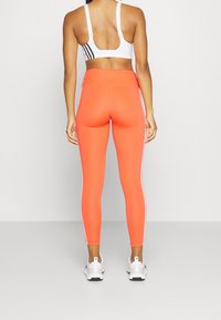 Klarröda högmidjade leggings med vita sidostråk, kombinerade med en vit sportbh. Tyget verkar elastiskt och kroppsnära.