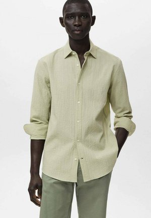 Lichtgroene blouse met lange mouwen, een gestructureerd patroon, een knopenrij aan de voorkant en opgerolde mouwen, gecombineerd met lichtgroene chinos.