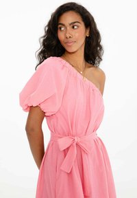 Rúžové šaty s jedným ramenom a balónovou rukávou, so zúženým pásom a detailom mašle. Vyrobené z ľahkej tkaniny, s mäkkou textúrou a voľným strihom.