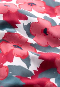 Röda och rosa blommor i akvarellstil med mörka mittpunkter på vit tyg, tillsammans med stora blågrå blad.