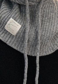 Szary prążkowany sweter z golfem o miękkiej fakturze, z czarnym korpusem i sznurkami do regulacji. Zawiera jasną metkę marki.