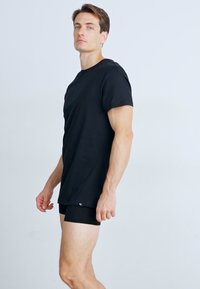 Black cotton t-shirt with short sleeves, round neckline, and a small logo accent. Paired with black briefs, showcasing a fitted look.