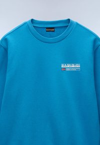 Cyaan blauwe sweatshirt van een katoenmix met een ronde halslijn. Bevat een klein, rechthoekig logo met tekst en vlagdetail op de borst.