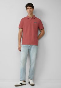 Polo shirt rosa con colletto e polsini a contrasto, abbinato a jeans azzurri chiari e sneakers bianche con dettagli neri.