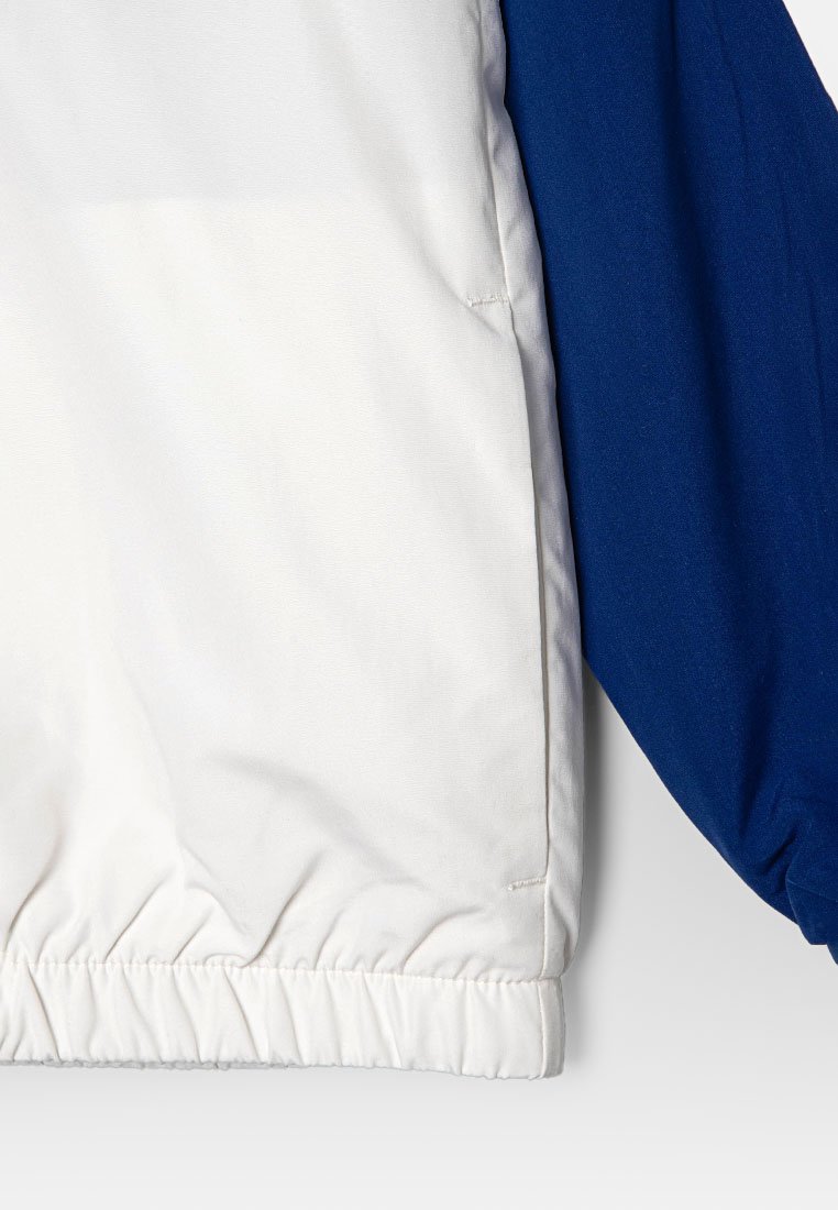 Veste colorée avec un corps blanc et des manches bleu roi. Tissu texturé avec un ourlet et des poignets élastiques, conçue pour un style ajusté.