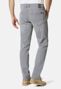 Graue Denim-Jeans mit Slim-Fit, fünf Taschen und kontrastierenden Nähten. Kombiniert mit beigen Ankle Boots auf einem weißen Hintergrund.