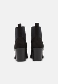 Botines de ante negro con tacón texturizado, paneles laterales elásticos y una lengüeta para facilitar su uso. Acabado liso y mate.