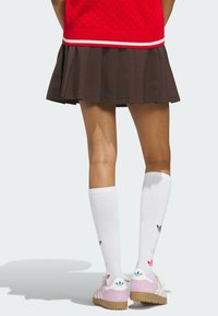 Pink sneakers with white stripes and logo at heel, paired with white knee-high socks featuring colored accents, and a pleated brown skirt.
