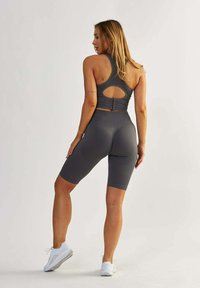 Szary zestaw sportowy składający się z TOPU na ramiączkach o otwartym plecach i teksturze prążkowanej, w zestawieniu z dopasowanymi szortami do kolan.