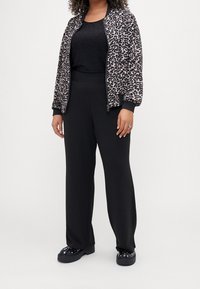 Kurtka bomberka w panterkę na czarnym błyszczącym topie, zestawiona z czarnymi szerokimi spodniami i masywnymi czarnymi butami. Teksturowany materiał i sportowy design.