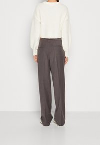 Weißer, strukturierter, verkürzter Pullover, kombiniert mit grauen, weiten Hosen mit zwei Gesäßtaschen und einer glatten Oberfläche.