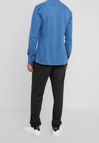 Camicia a maniche lunghe blu in tessuto morbido con polsini abbottonati, abbinata a pantaloni grigio scuro e sneakers bianche. Design semplice e casual.