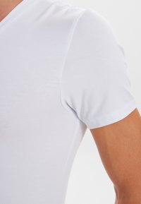 Witte T-shirt met korte mouwen van rekbare, gladde stof met een V-hals ontwerp en een aansluitende silhouet. Naaddetails bij de schouders.