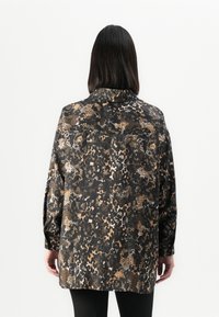 Maglietta nera con design a stampa animale in tonalità beige e marrone, con colletto e maniche lunghe, mostrata da dietro.