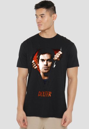 Man wears black shirt featuring graphic of a man tearing through fabric with red background and "Dexter" text at bottom.