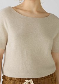 Haut en maille beige à manches courtes avec un décolleté large et arrondi, texture lisse et coupe décontractée, associé à un pantalon beige à cordon de serrage.