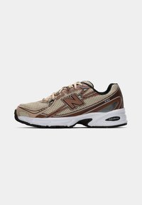 Chaussure de course New Balance beige et marron avec dessus en mesh, languette rembourrée et semelle extérieure en caoutchouc. Caractéristiques des accents texturés et un coussin en milieu de semelle.