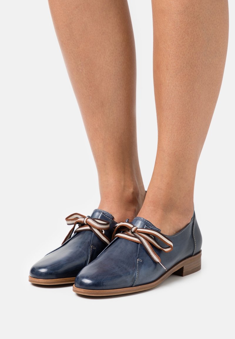Chaussures en cuir bleu marine avec un bout rond, un talon plat et des lacets marron clair. Présente des détails de couture et une finition lisse.