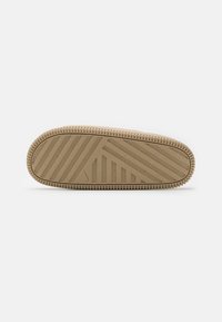 Tan rubber shoe sole with textured horizontal and diagonal grooves, featuring a circular edge and small logo detail.